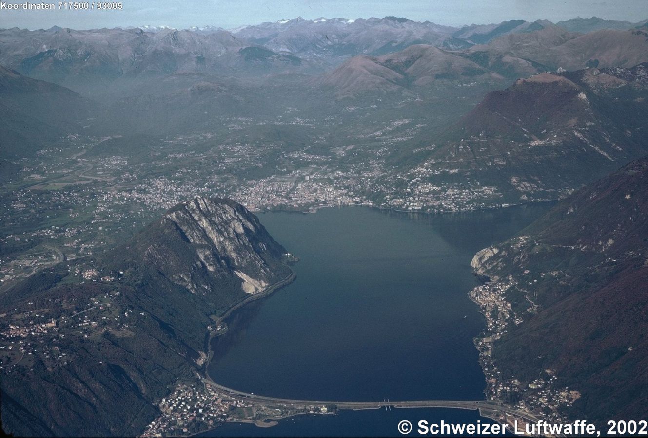 Blick über den Damm von Melide nach Lugano. Aussichtsberg Bildmitte links am See: Monte San Salvatore (887 m.ü.M.) Am östlichen See-Ufer: italienische Exklave Campione. Im Bildzentrum: Lugano. Erhebung östlich (rechter Bildrand, obere Mitte): Siedlung 'Brè sopra Lugano' (Postion 2'720'718.78, 1'096'778.48) am Monte Boglia und Colma Regia.